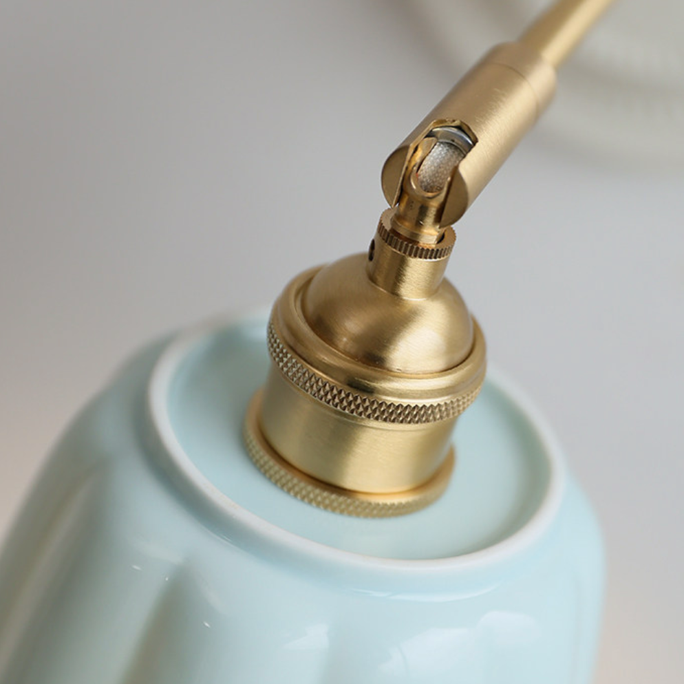 Close-up of a light blue ceramic pump bottle with a polished brass pump dispenser, showing the nozzle and adjustment collar against a soft neutral background.