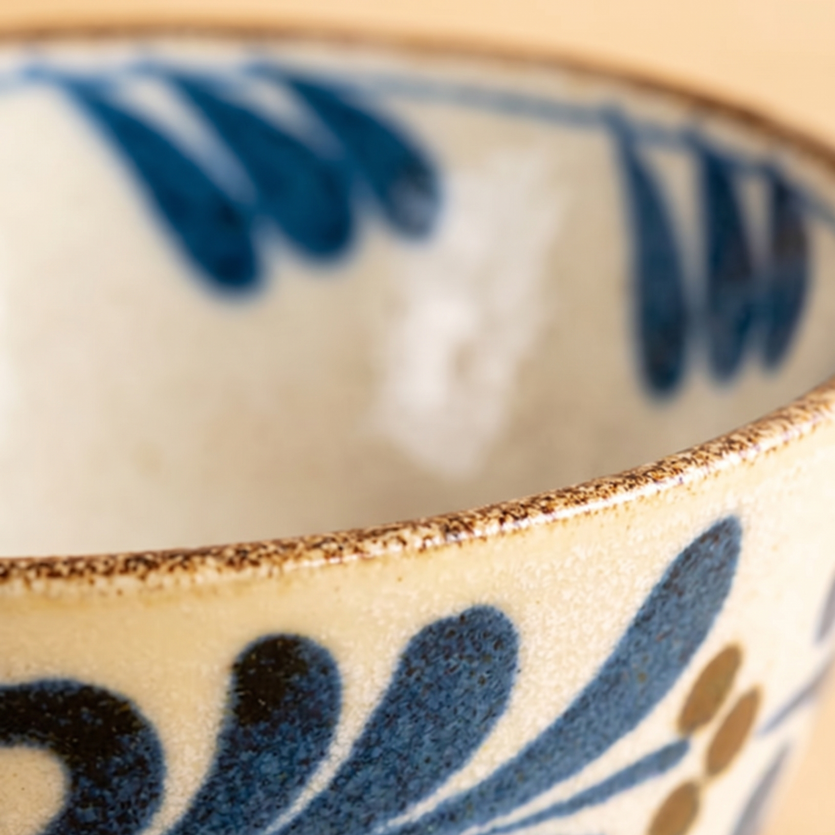 Close-up of a ceramic bowl with a cream-colored glaze, dark blue floral pattern, and a rustic brown rim.
